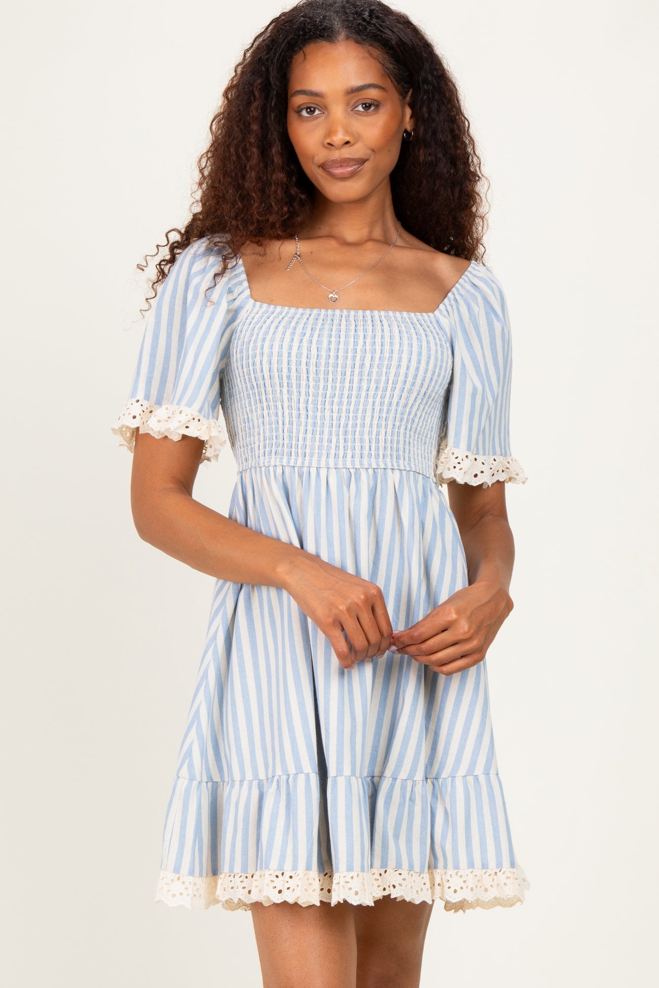 woman wearing a light blue striped short sleeve dress with smocking and lace trim details