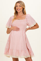 woman wearing a pink and white striped maternity dress with smocked bodice and lace trim on sleeves and hem