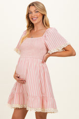 woman wearing a pink and white striped maternity dress with smocked bodice and lace trim, showing her baby bump