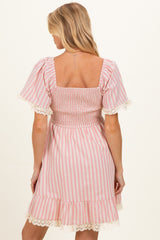 woman wearing a pink and white striped maternity dress with smocked bodice and lace trim on sleeves