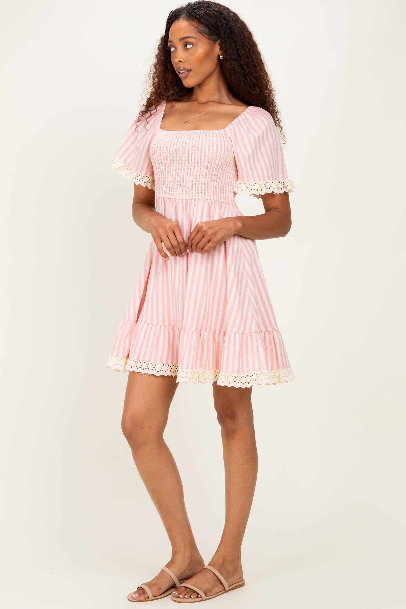 woman wearing a pink and white striped short dress with a square neckline and lace trim at the sleeves and hem