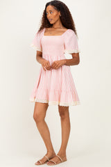 woman wearing a pink and white striped short dress with a square neckline and lace trim at the sleeves and hem