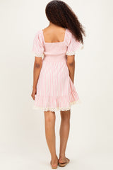 woman wearing a pink and white striped puff sleeve dress with a tiered hem and lace trim, viewed from the back