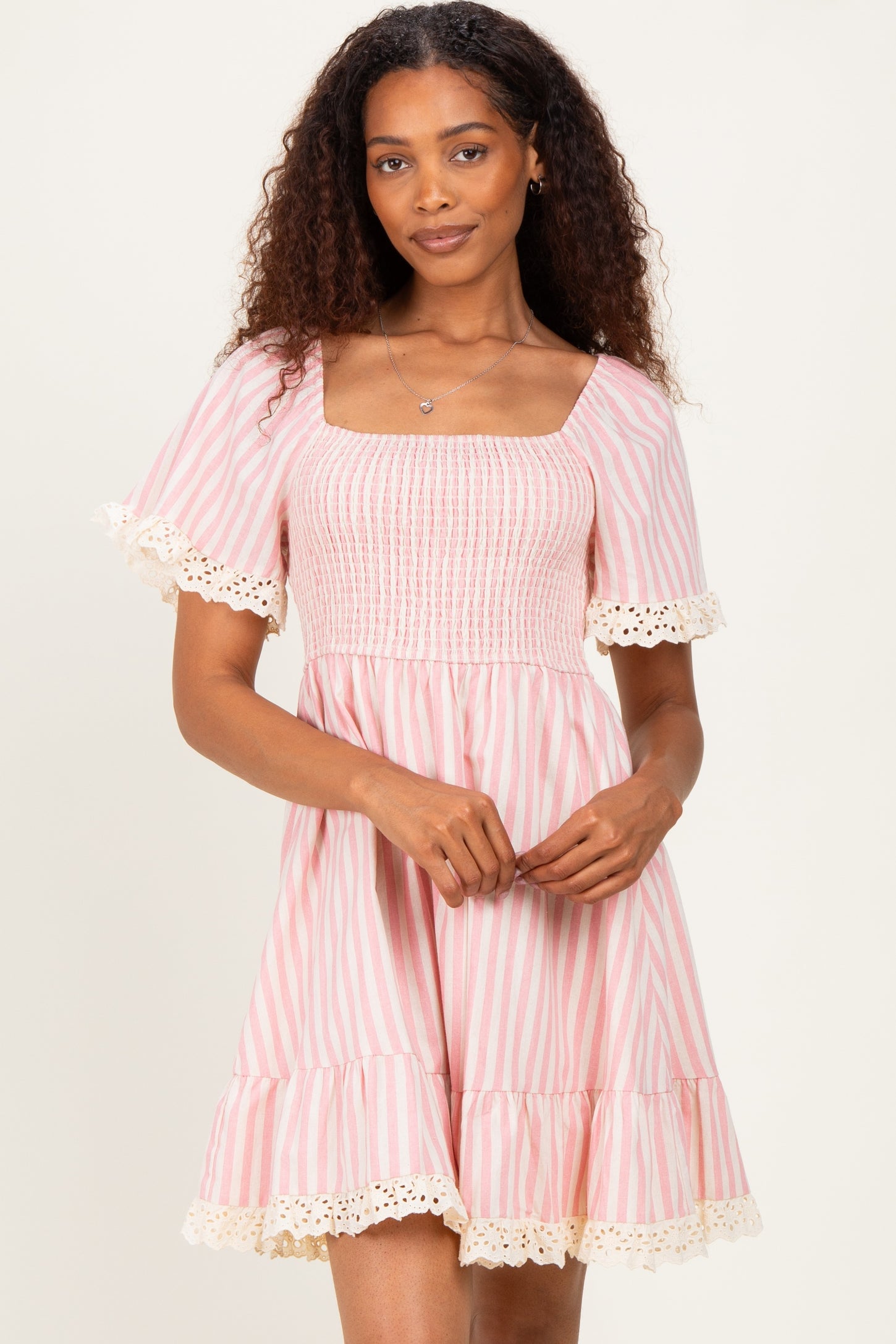 woman wearing a pink and white striped smocked dress with short sleeves and lace trim at the hem