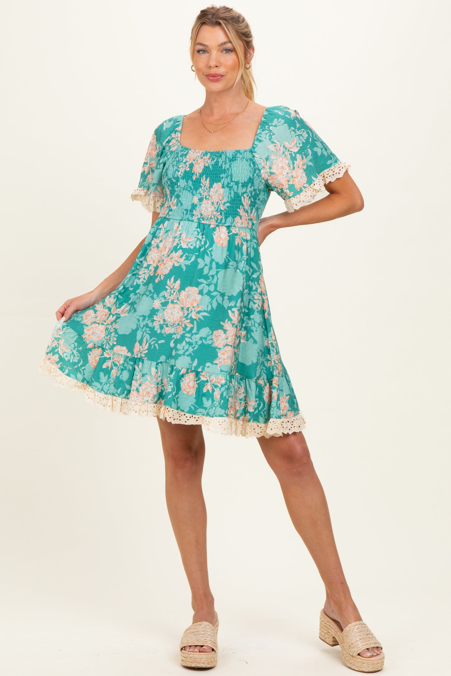 woman wearing a teal floral maternity dress with short ruffled sleeves and lace trim, showing off her baby bump