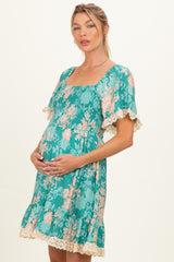 woman wearing a teal floral print maternity dress with smocked bodice and lace trim, cradling her baby bump
