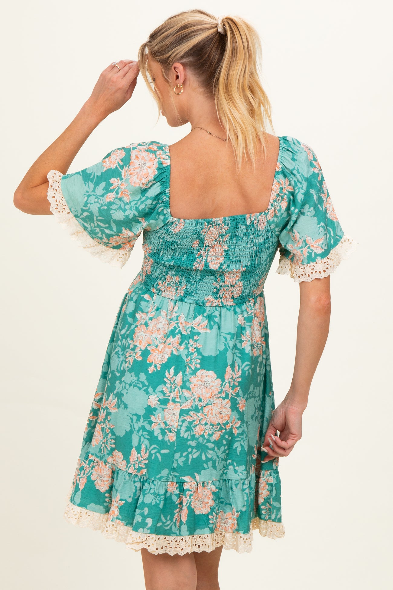 woman wearing a green floral maternity dress with a smocked bodice and lace trim on the sleeves