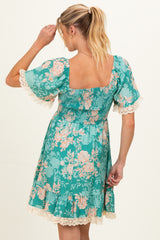 woman wearing a green floral maternity dress with a smocked bodice and lace trim on the sleeves
