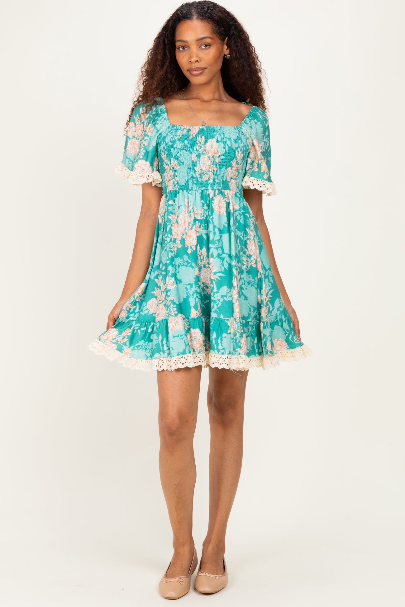 woman wearing a teal floral short dress with a smocked bodice and lace trim on the sleeves and hem