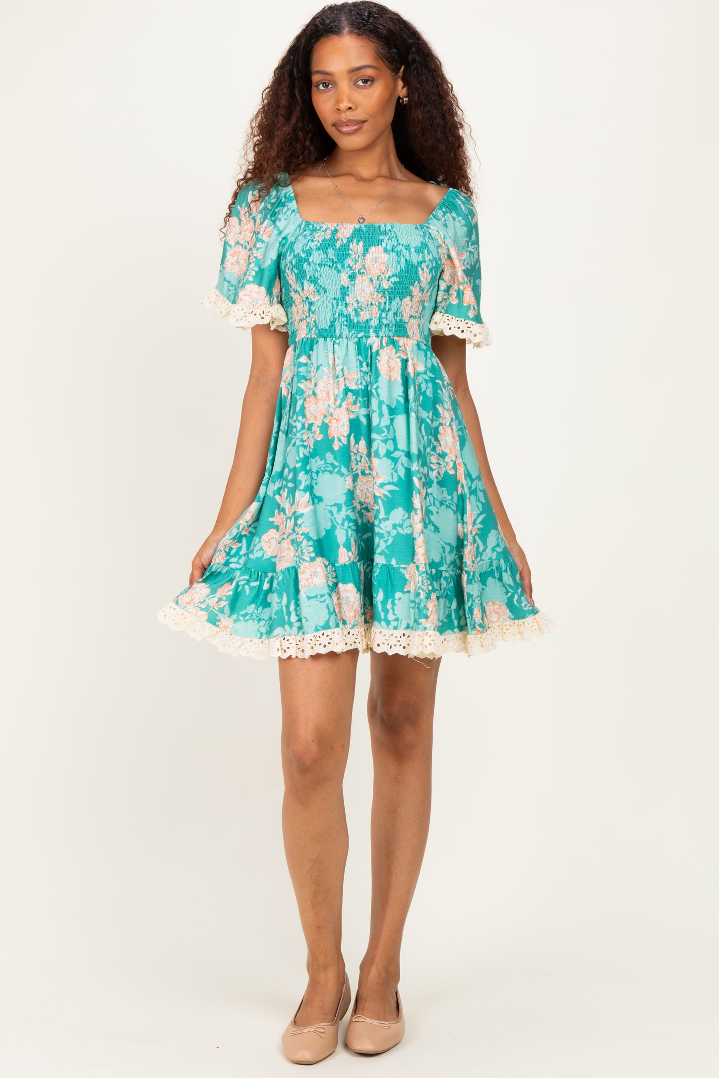woman wearing a teal floral short dress with a smocked bodice and lace trim on the sleeves and hem