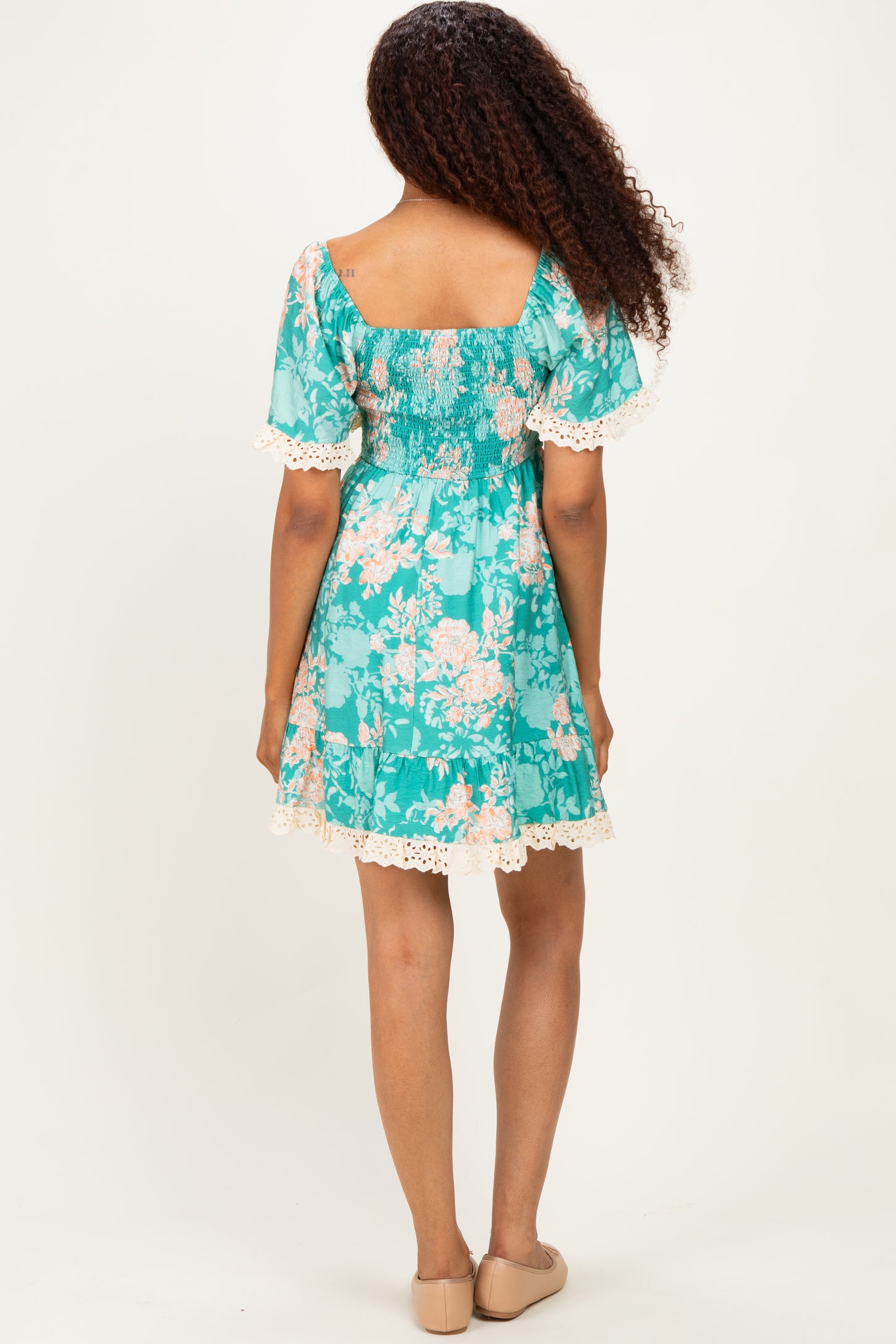woman wearing a teal floral dress with short sleeves and lace trim, viewed from the back