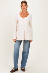 woman wearing a light beige long sleeve maternity top with button details and a baby bump, paired with blue jeans