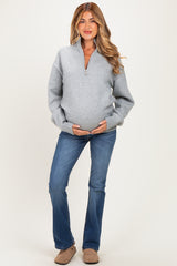 woman wearing a light gray maternity pullover sweater and blue flared jeans, holding her baby bump