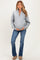 woman wearing a light gray maternity pullover sweater and blue flared jeans, holding her baby bump