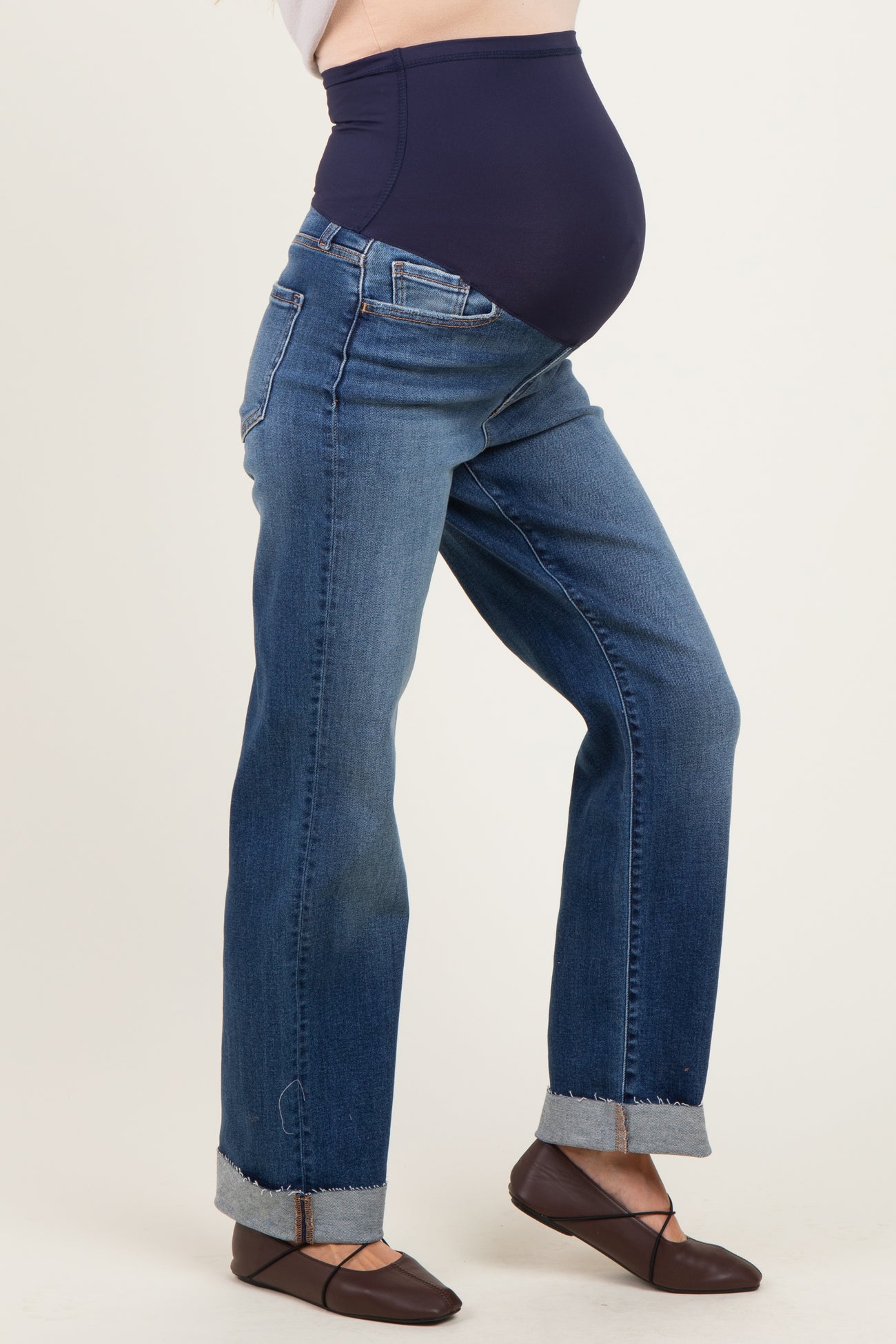 woman wearing maternity dark wash straight leg jeans with a navy over-the-bump waistband and cuffed hems, baby bump visible