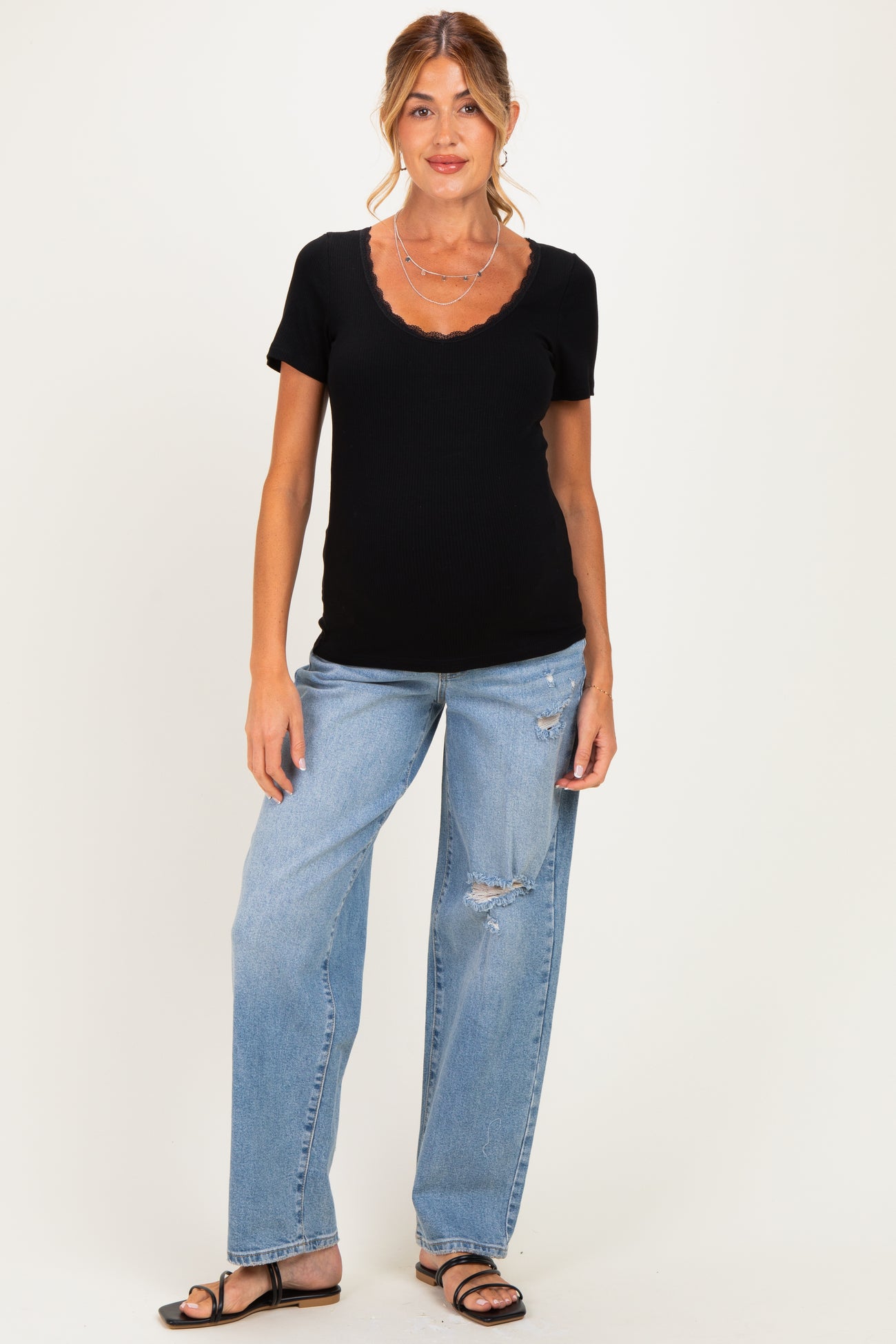 woman wearing a black maternity top with a scalloped neckline and paired with distressed light blue jeans