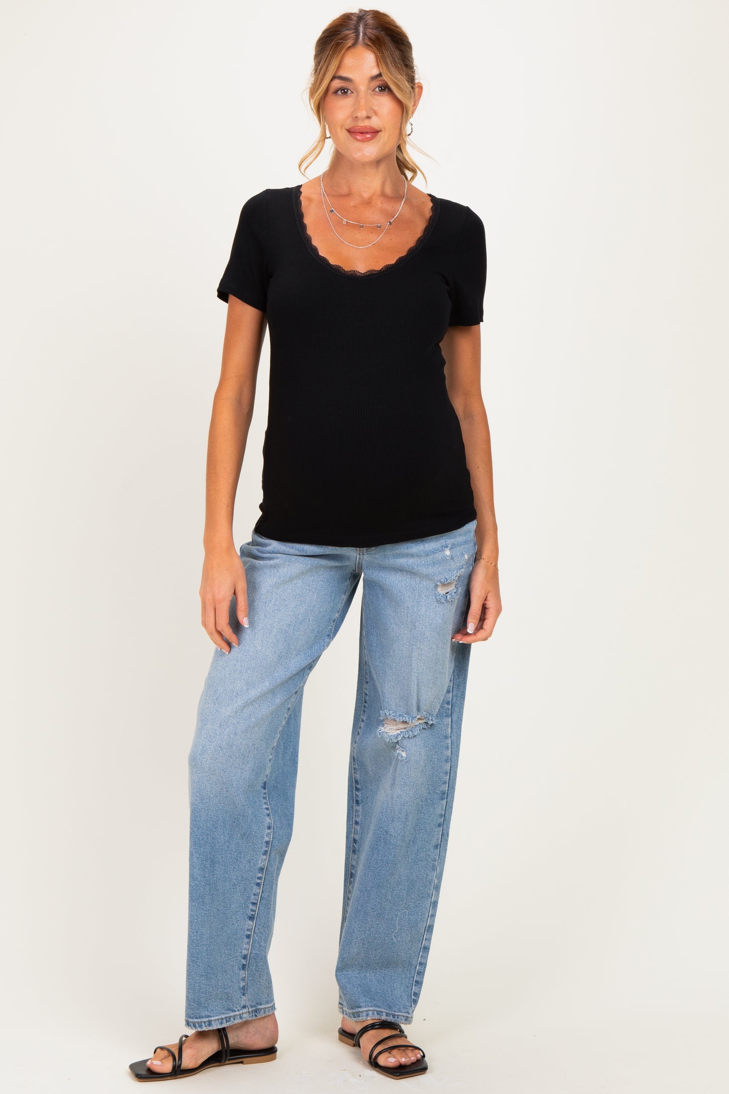 woman wearing a black maternity top with a scalloped neckline and paired with distressed light blue jeans