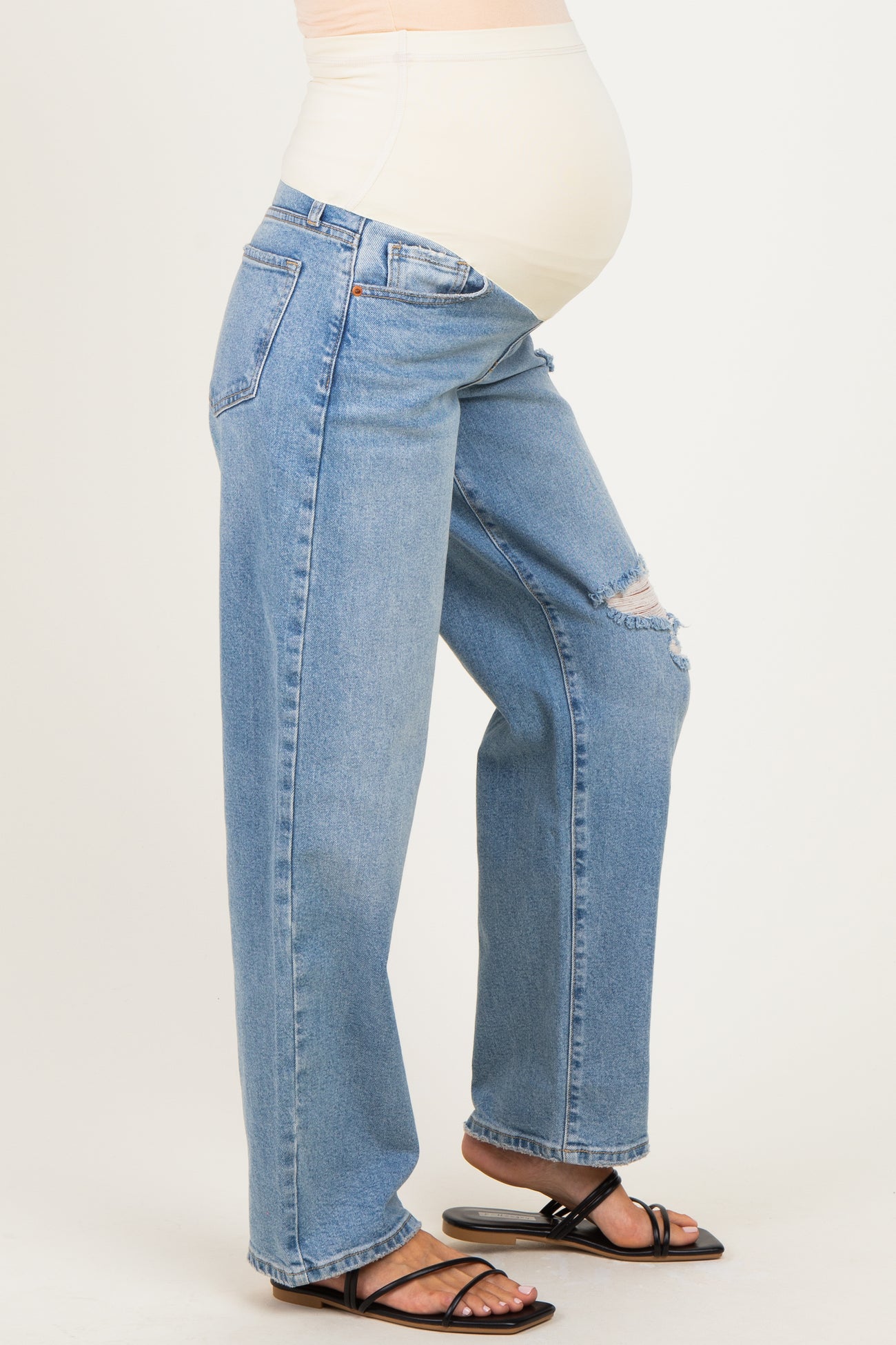 woman wearing light blue maternity jeans with a relaxed fit and distressed details, showing her baby bump