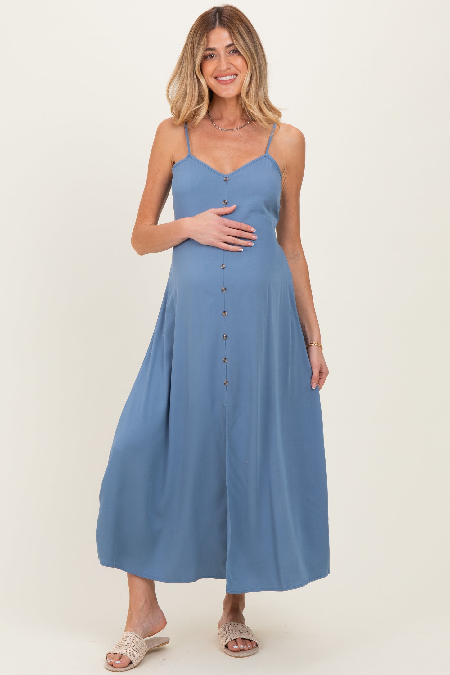 woman wearing a blue sleeveless maternity maxi dress with buttons and holding her baby bump
