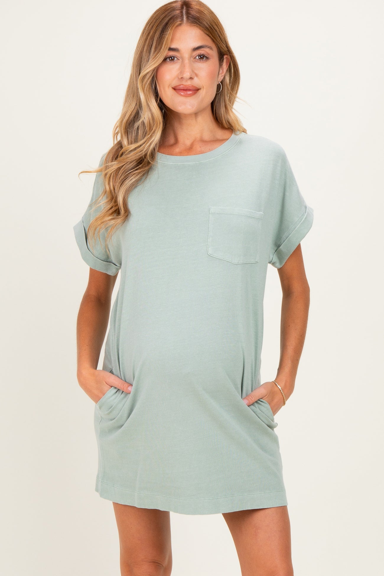 woman wearing a light green maternity t-shirt dress with rolled sleeves and side pockets, showing her baby bump