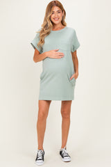 woman wearing a light green maternity dress with a pocket and rolled sleeves, holding her baby bump