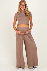 woman wearing a taupe short sleeve crop top and matching wide-leg maternity pants, holding her baby bump