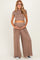 woman wearing a taupe short sleeve crop top and matching wide-leg maternity pants, holding her baby bump