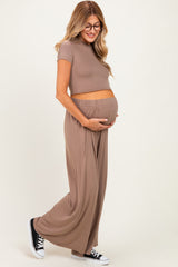woman wearing a brown short sleeve maternity top and matching flowy maternity pants with a visible baby bump