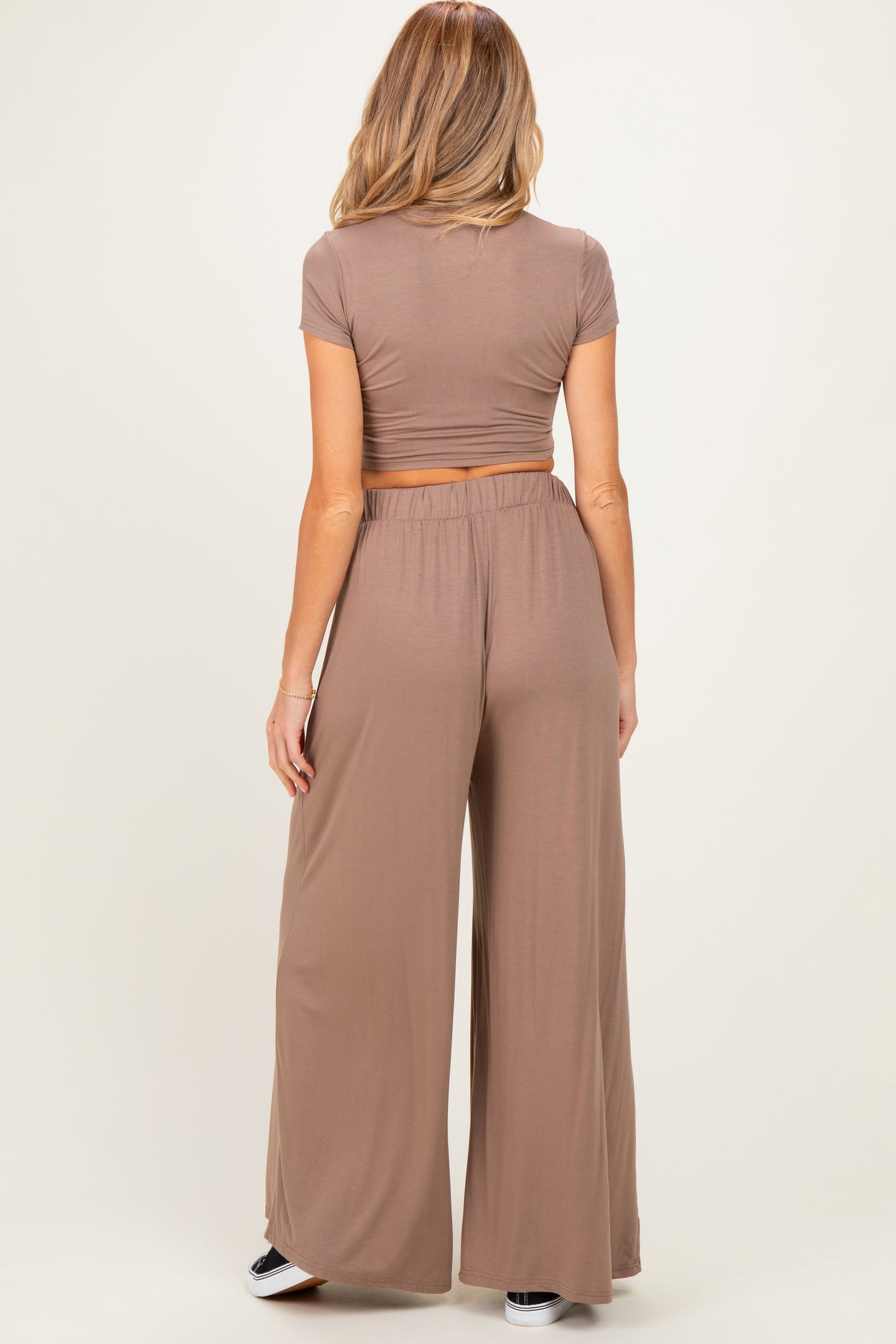 woman wearing a brown maternity crop top and wide-leg pants, showing a small baby bump from the back