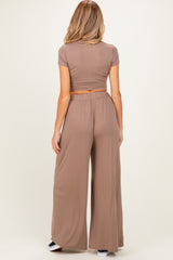 woman wearing a brown maternity crop top and wide-leg pants, showing a small baby bump from the back