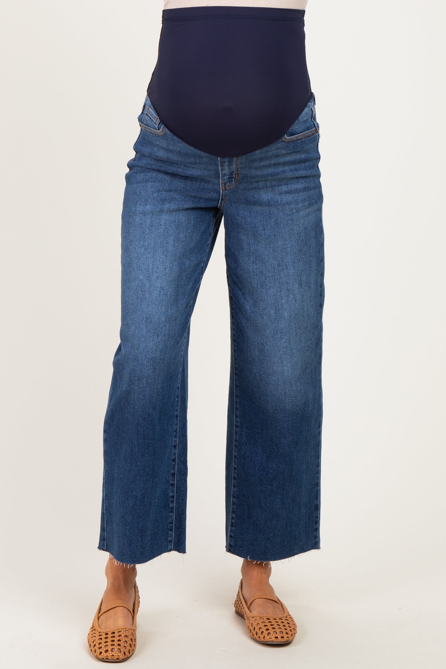 woman wearing dark blue maternity jeans with a high waistband and frayed hem, paired with brown flat sandals