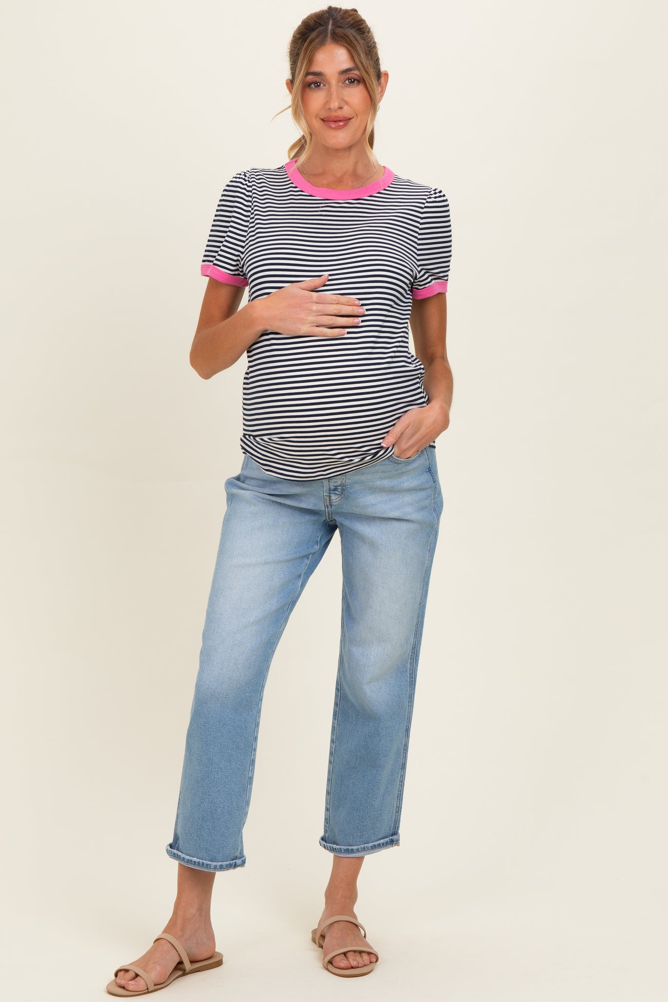 woman wearing a black and white striped maternity top with pink trim and blue maternity jeans, holding her baby bump