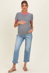 woman wearing a black and white striped maternity top with pink trim and blue maternity jeans, holding her baby bump