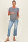 woman wearing a black and white striped maternity top with pink trim and blue maternity jeans, holding her baby bump