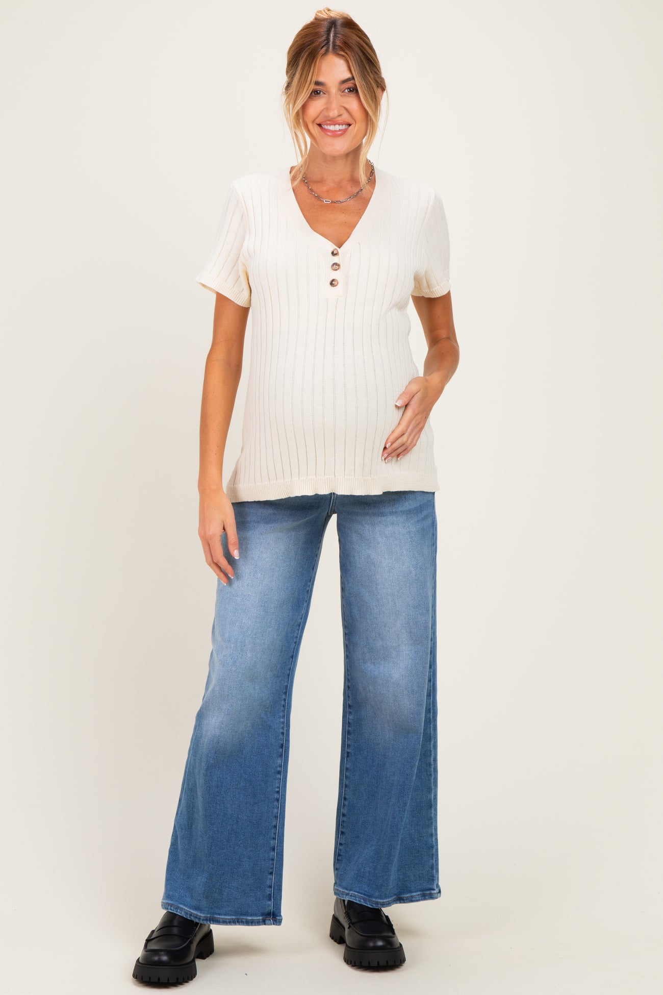 woman wearing a cream ribbed maternity top with buttons and light blue wide-leg jeans, highlighting her baby bump