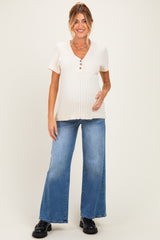 woman wearing a cream ribbed maternity top with buttons and light blue wide-leg jeans, highlighting her baby bump
