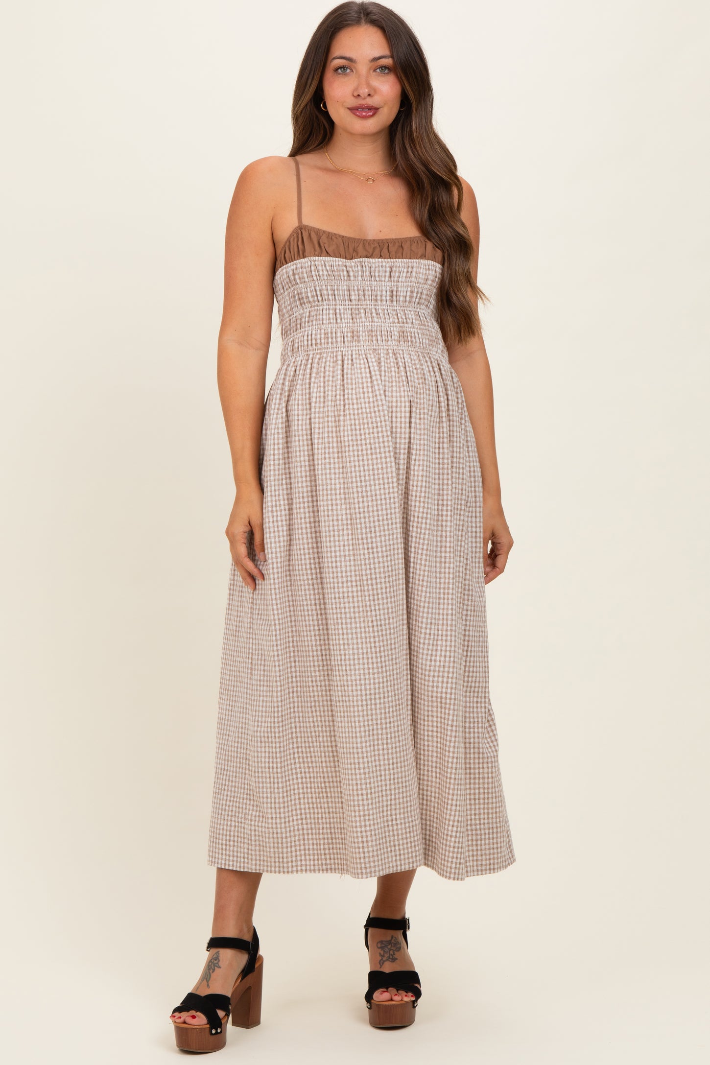 woman wearing a brown and white gingham maternity dress with smocked bodice and adjustable spaghetti straps