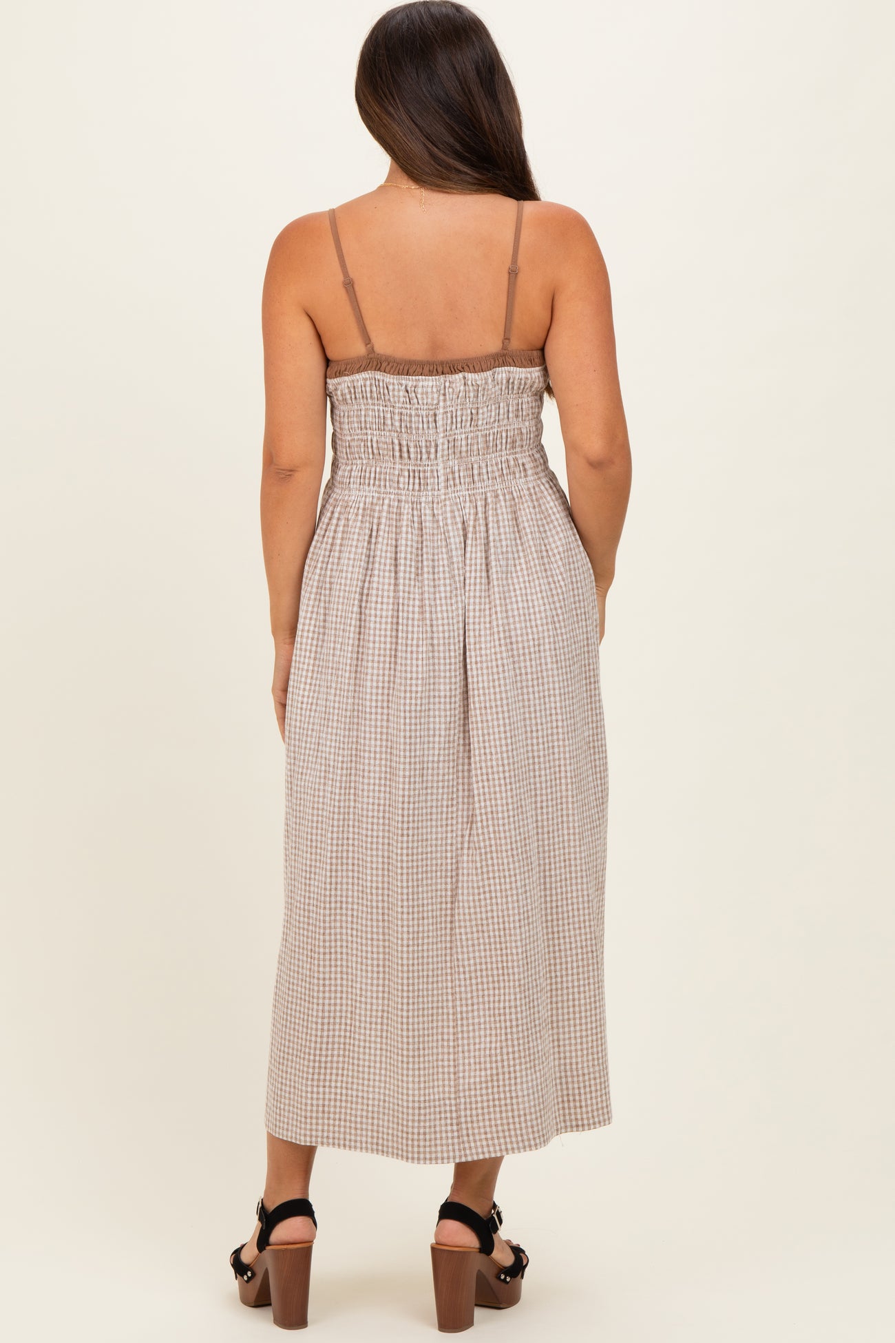 woman wearing a brown and cream checked maternity maxi dress with a smocked back and adjustable straps