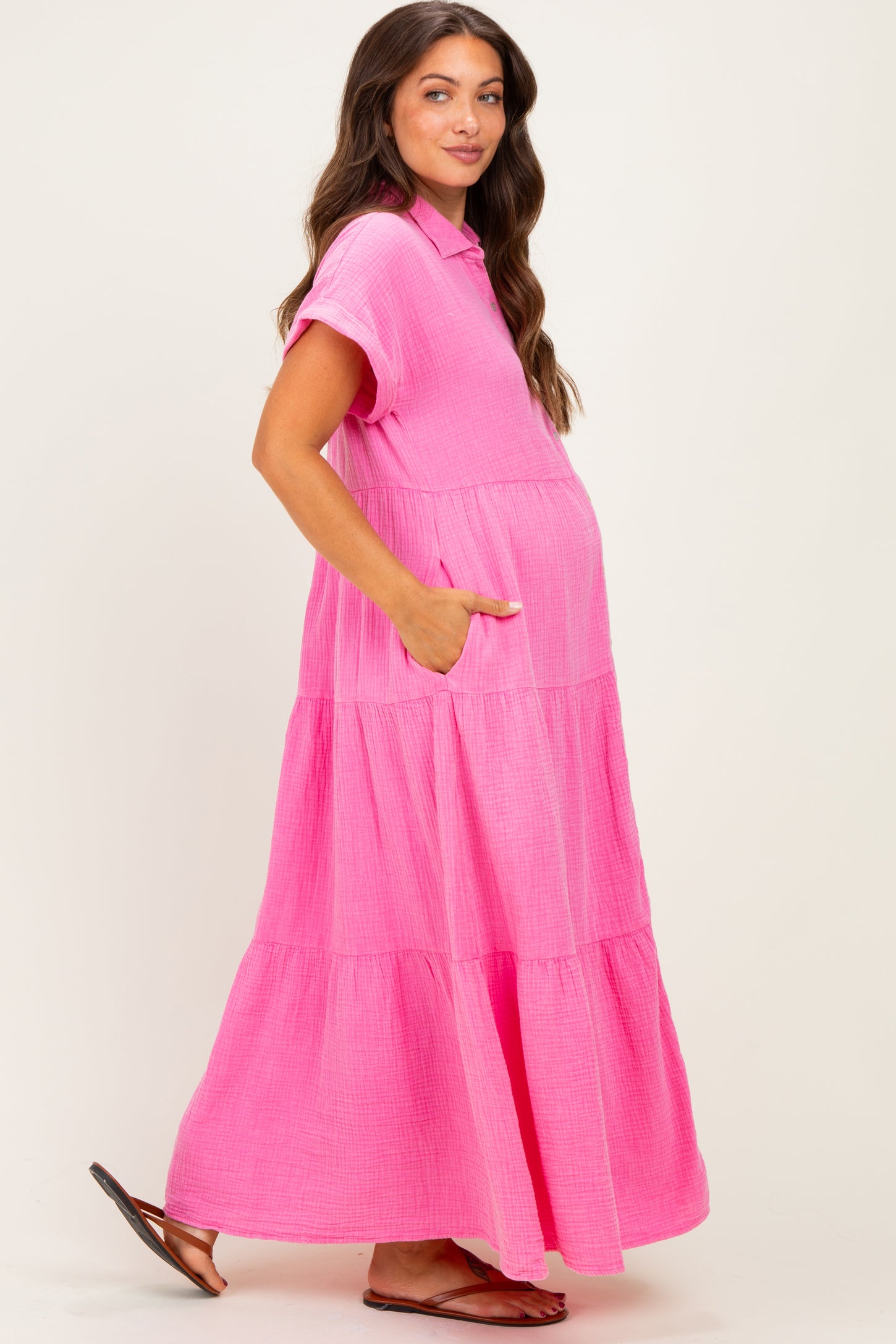 woman wearing a hot pink tiered maternity maxi dress with short sleeves and pockets, showcasing her baby bump