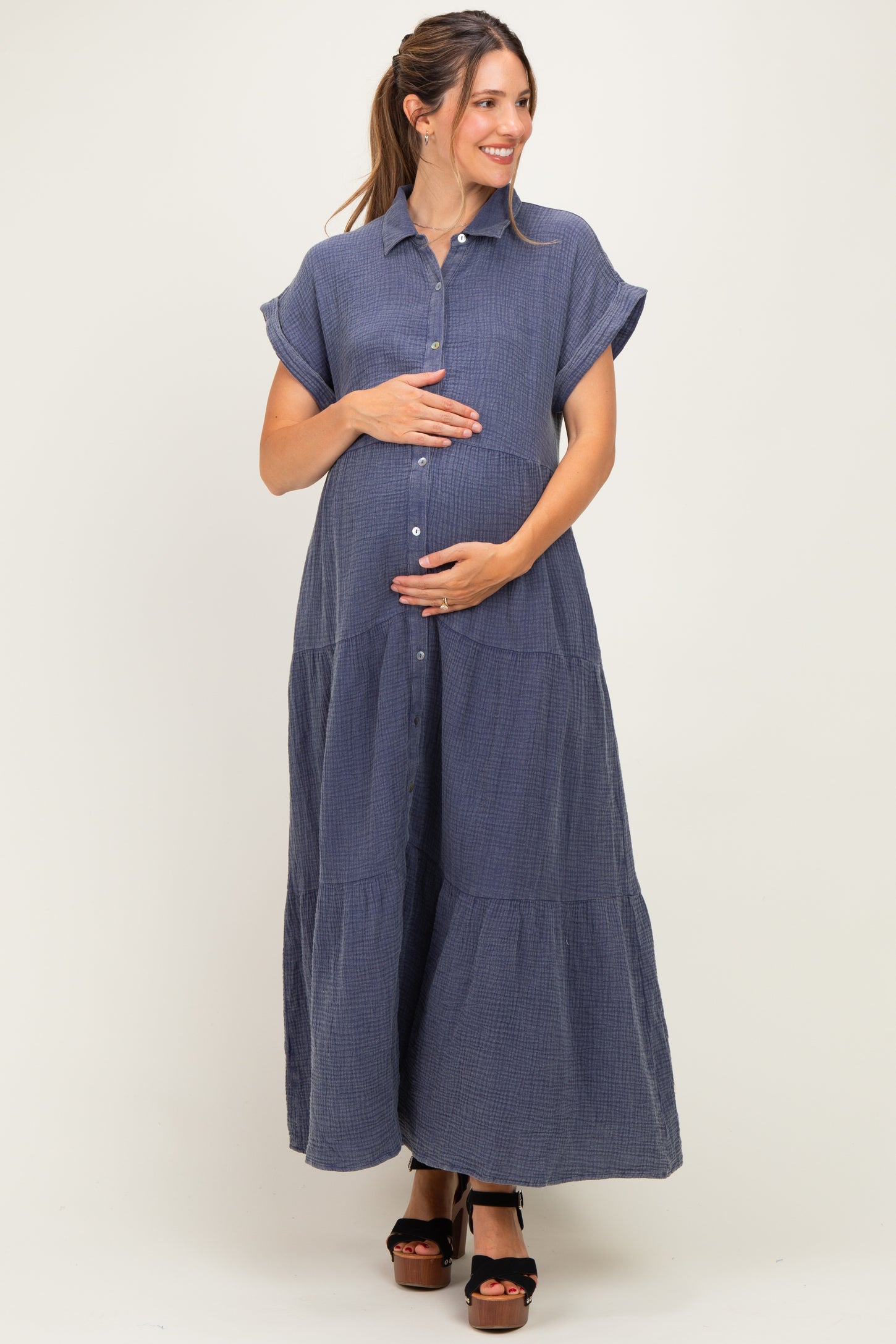 woman wearing a navy blue short sleeve button-down maternity maxi dress and holding her baby bump