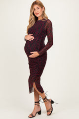 woman wearing a red polka dot maternity dress with long sheer sleeves and a side slit, holding her baby bump