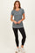 woman wearing a gray short sleeve fitted top with a round neck and black leggings, standing with hands on her hips