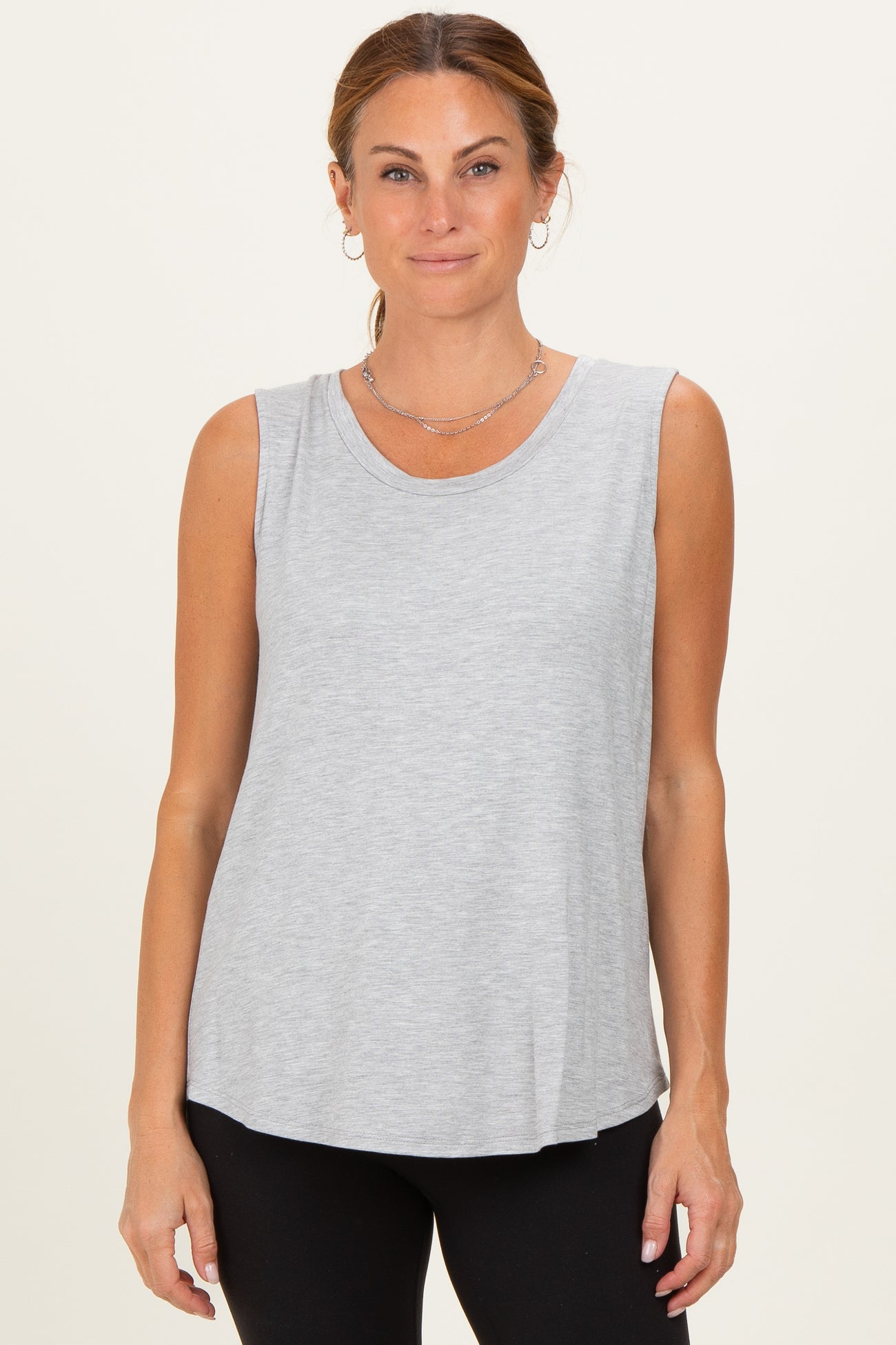 woman wearing a light gray sleeveless top with a rounded neckline and relaxed fit, styled with black leggings