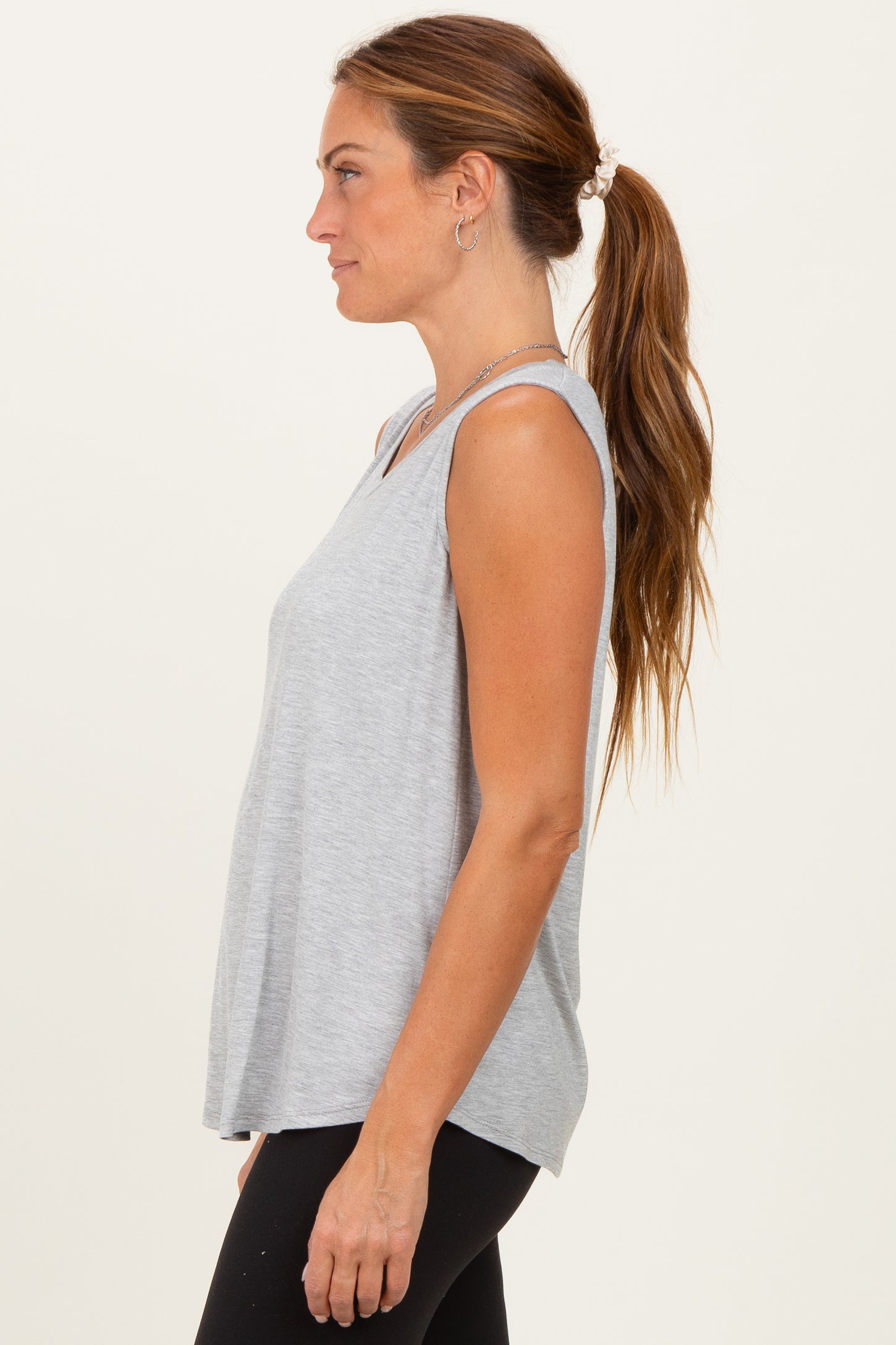 woman wearing a gray sleeveless top with a relaxed fit and side slits, paired with black leggings