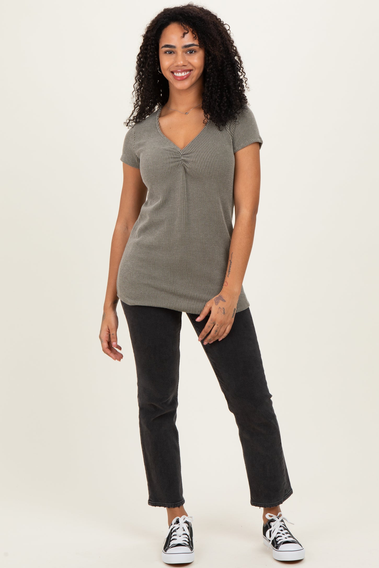 woman wearing a green ribbed short sleeve top and black high-waisted jeans, standing with a smile