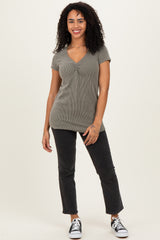 woman wearing a green ribbed short sleeve top and black high-waisted jeans, standing with a smile