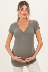 woman wearing a grey ribbed maternity top with a v-neck and short sleeves, holding her baby bump