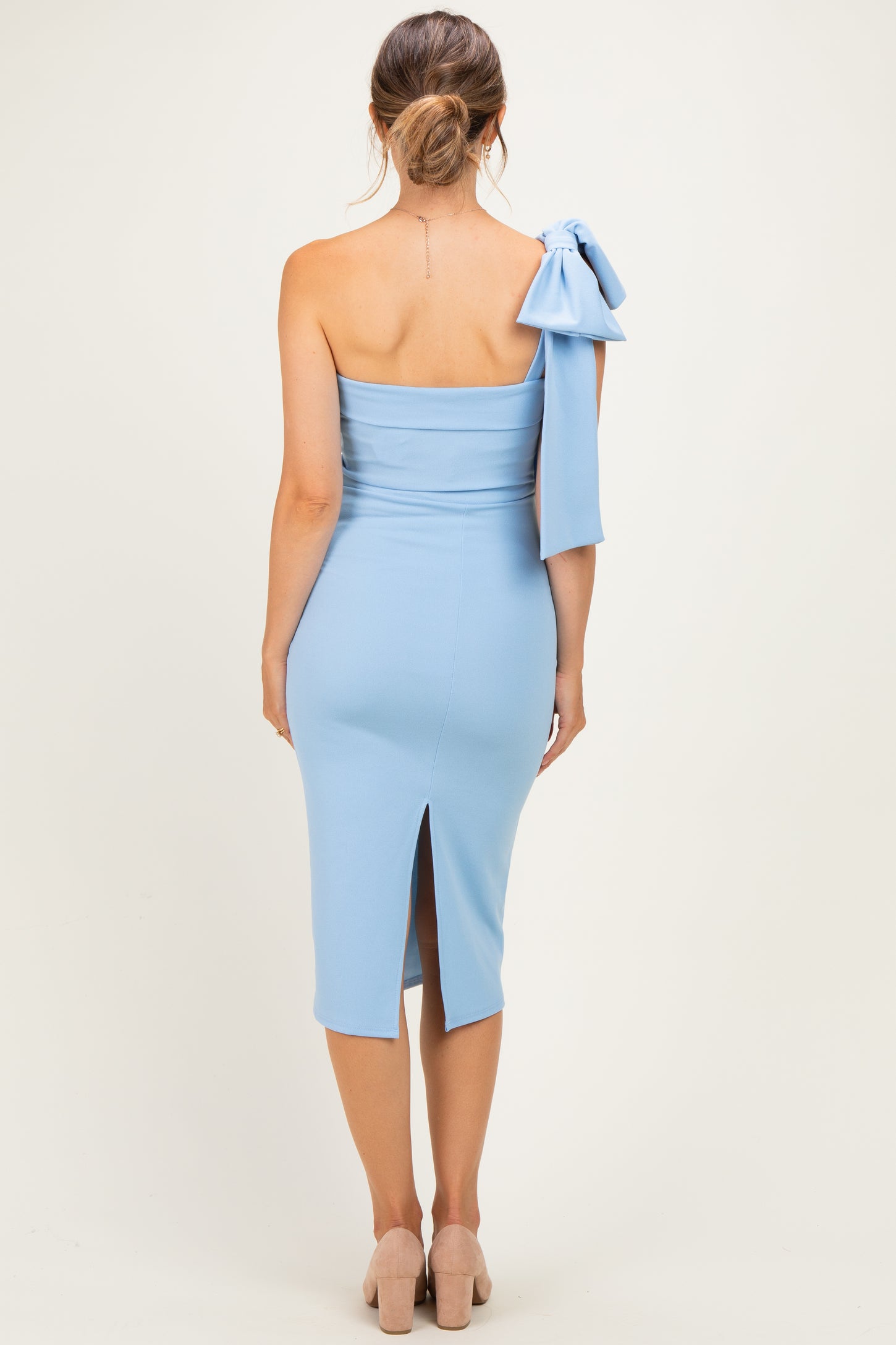 woman wearing a light blue one-shoulder maternity dress with a bow detail on the sleeve and a back slit