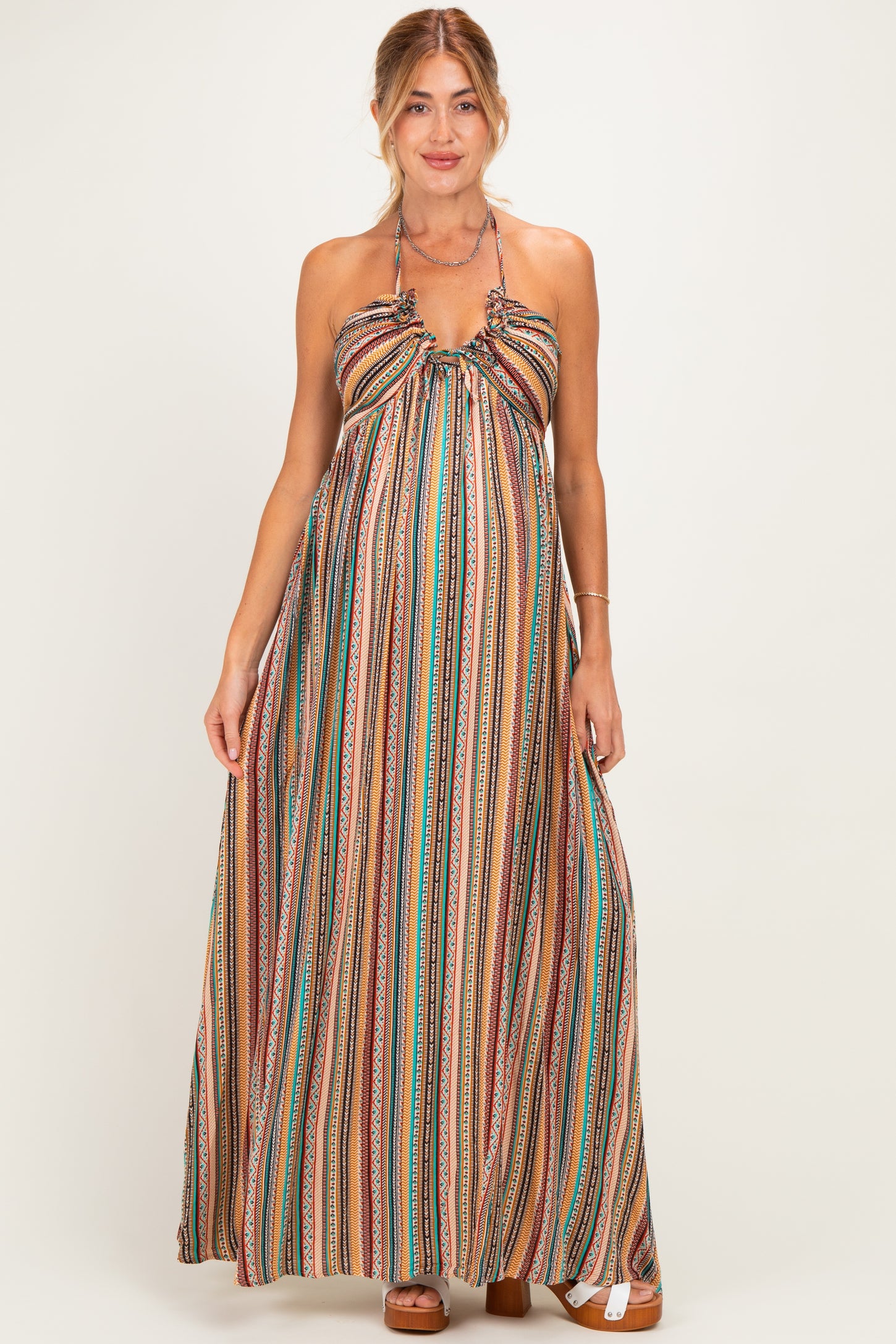 woman wearing a multicolored striped maternity maxi dress with a halter neck and flowing silhouette, showcasing her baby bump