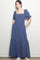 woman wearing a navy blue maxi dress with square neckline and puff sleeves, standing with hands in pockets
